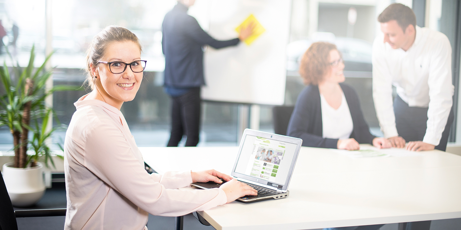 Woman sitting at a desk, two colleagues in the background.